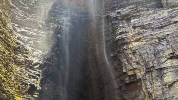 Een waterval stort neer over een rotswand, met een persoon die op een rotsformatie aan de voet staat.