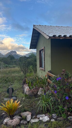 A house with a green exterior and a tiled roof, surrounded by a garden with various plants and flowers. - Hospedaria Portal das Montanhas  (Ibicoara)