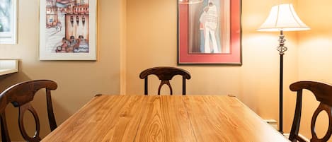 A dining area with a wooden table, chairs, a lamp, and two framed artworks on the wall.