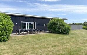 Un edifici modern amb façana fosca, un pati amb taula i cadires, i vegetació ben cuidada.