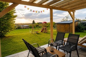 A covered patio with outdoor furniture, a swing set, and a playhouse in the background. - Wooden holiday home with a heated indoor saltwater pool near Vrbovec (Vrbovec)