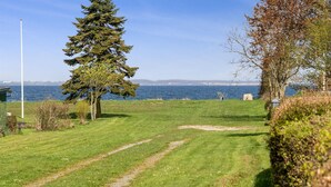 A grassy area with a path leading to a body of water, a flagpole, and a bench.