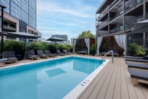 A rooftop pool with lounge chairs and umbrellas, surrounded by modern buildings. - Upscale Condo in Downtown with Pool, Balcony, Gym + Garage (Nashville)