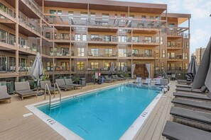 Ein mehrstöckiges Hotel mit Poolbereich auf dem Dach, inklusive Liegestühlen und Sonnenschirmen.
