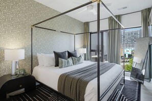 A modern hotel room with a four-poster bed, a view of the city, and a large window with curtains. - Upscale Condo in Downtown with Pool, Balcony, Gym + Garage (Nashville)