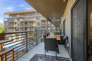 Ein Balkon mit Tisch und Stühlen, ein Schwimmbad und ein mehrstöckiges Gebäude im Hintergrund.