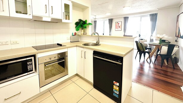 Een moderne keuken met witte kasten, een ingebouwde oven, een vaatwasser en een eethoek met een tafel en stoelen.