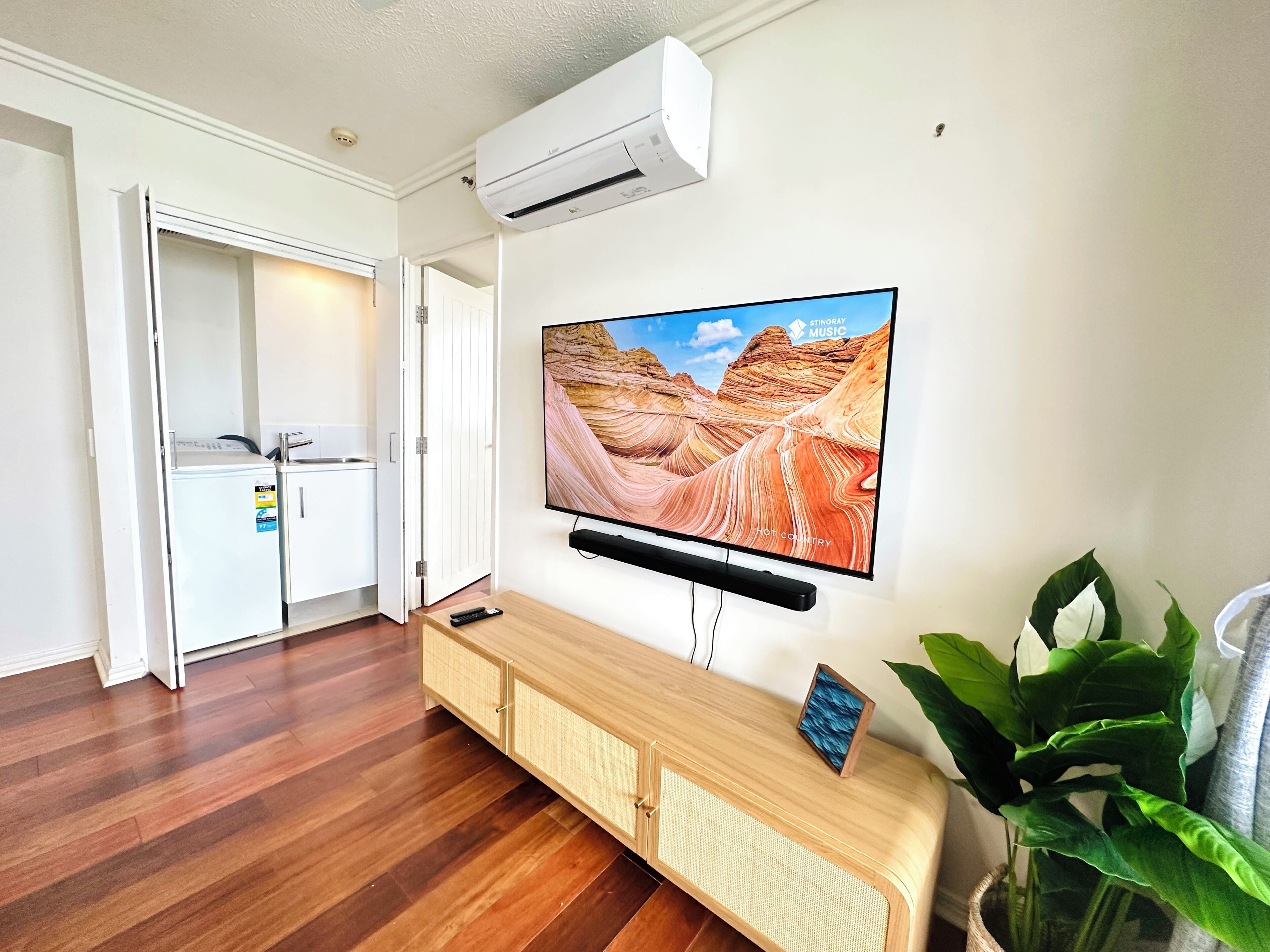 Ein modernes Wohnzimmer mit einem Wand-Fernseher, der eine Schluchtlandschaft zeigt, einem Holzkonsolentisch und einer Topfpflanze.