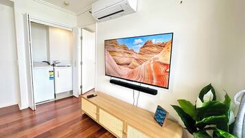 Ein modernes Wohnzimmer mit einem Wand-Fernseher, der eine Schluchtlandschaft zeigt, einem Holzkonsolentisch und einer Topfpflanze.