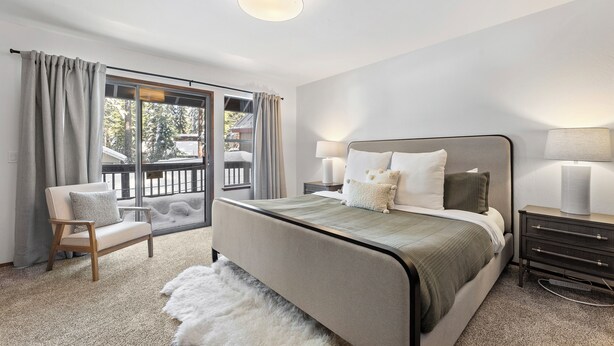 Un dormitorio con cama, mesitas de noche, una silla, una ventana con cortinas y vistas a un paisaje nevado.
