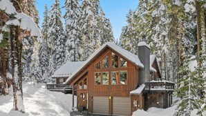 Una cabaña de madera con garaje, rodeada de árboles cubiertos de nieve.