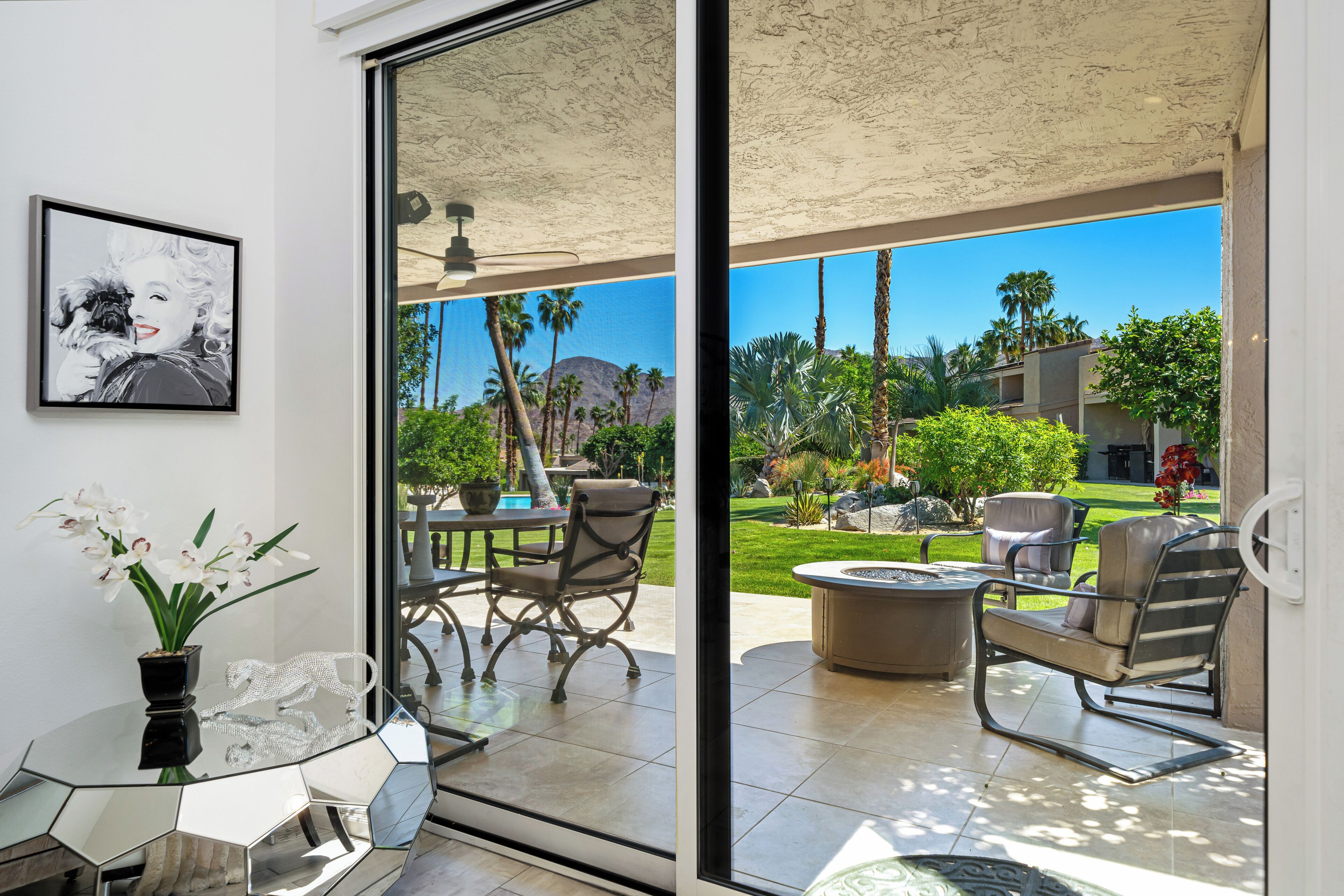 Une terrasse moderne avec une porte vitrée donnant sur un espace piscine, du mobilier d’extérieur et une vue sur un jardin aménagé.