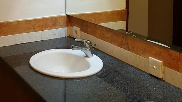 Une salle de bain avec un lavabo blanc, un miroir et un luminaire placé au-dessus du miroir.