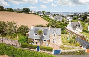 A stone house with a sloped roof, surrounded by lush greenery and a view of the sea. - Amazing home in Ploubazlanec with WiFi (Ploubazlanec)