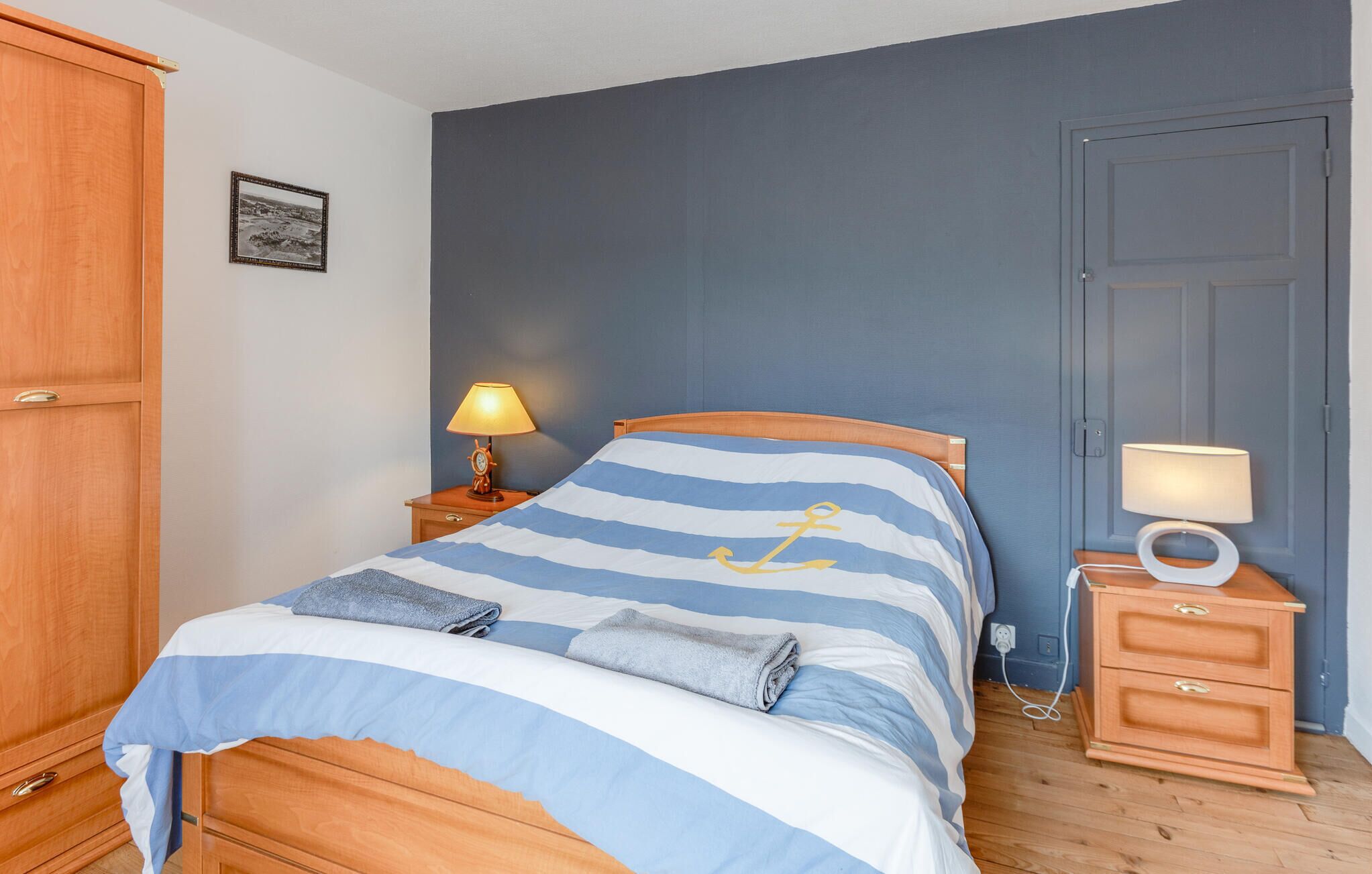 A bedroom with a bed, a nightstand, a lamp, a wardrobe, and a door.