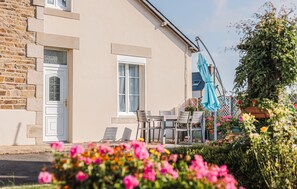 Ein Gebäude mit einer Stein-Fassade, einer Tür und Fenstern. Eine Terrasse mit Stühlen und einem Tisch sowie einem blauen Sonnenschirm.