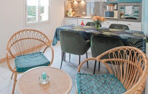 Un coin repas avec des chaises en osier, une table ronde et une cuisine en arrière-plan.