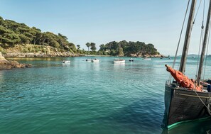Eine ruhige Bucht mit mehreren vor Anker liegenden Booten, klarem türkisblauem Wasser und einer felsigen Küste mit Bäumen.