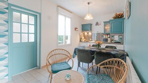 Een compacte keuken met een eethoek, met een ronde tafel, rieten stoelen en teal kastjes.