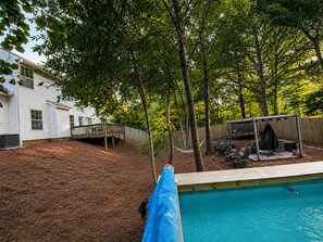 Ein Garten mit Swimmingpool, einer Holzterrasse und einer Hängematte.
