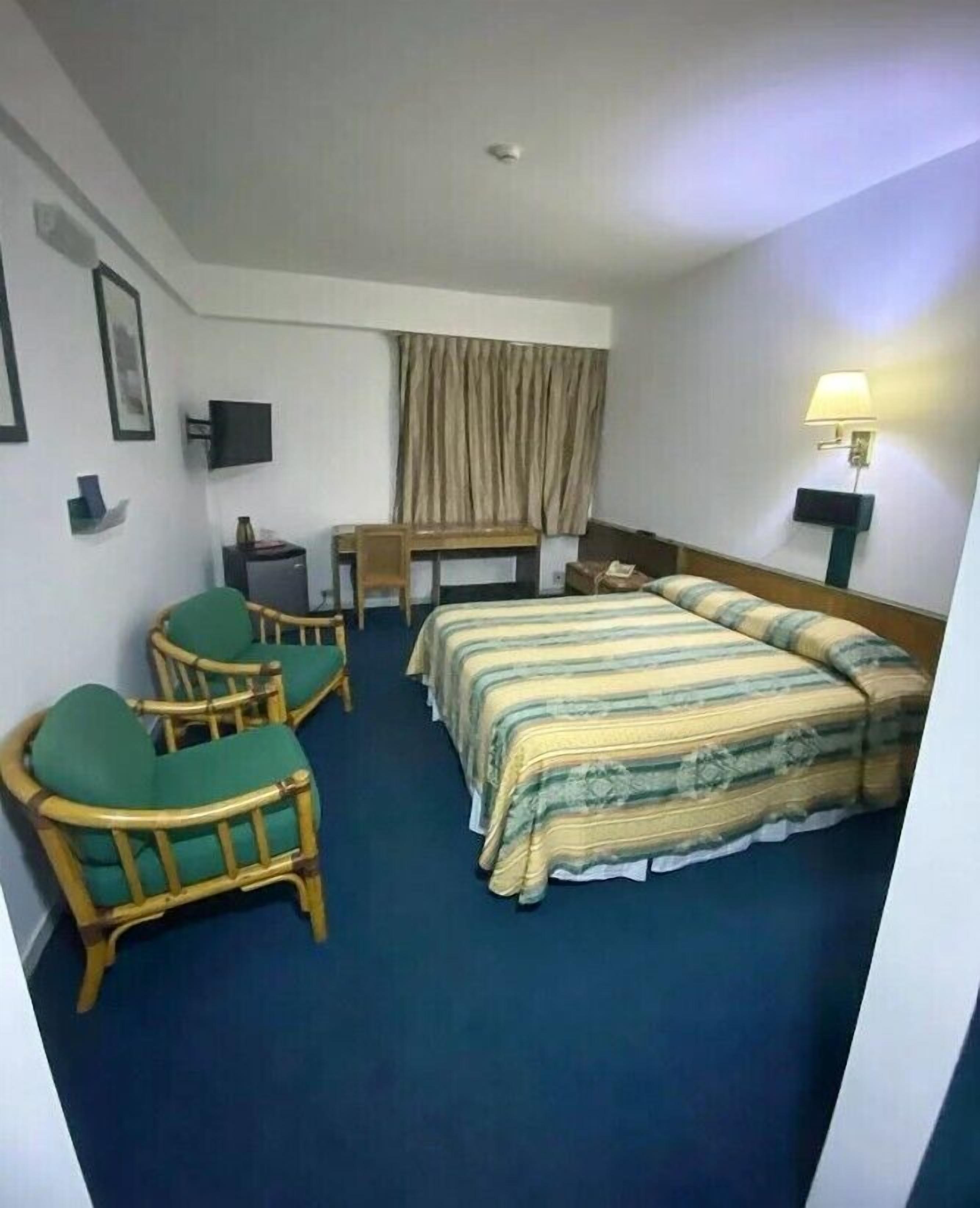 A hotel room with a bed, two chairs, a desk, a television, and a lamp.