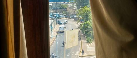 A window with curtains, through which a cityscape with buildings, roads, and vehicles is visible.