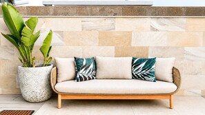 A beige sofa with two pillows, a large potted plant, and a stone wall.