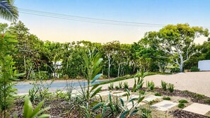 A landscaped outdoor area with a variety of plants and trees, a paved walkway, and a clear sky.