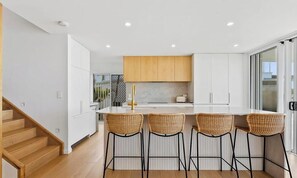 Une cuisine moderne avec des meubles blancs, un îlot central doté de tabourets de bar et un escalier en bois.