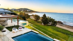 A modern house with a swimming pool, a covered patio, and a view of the sea.