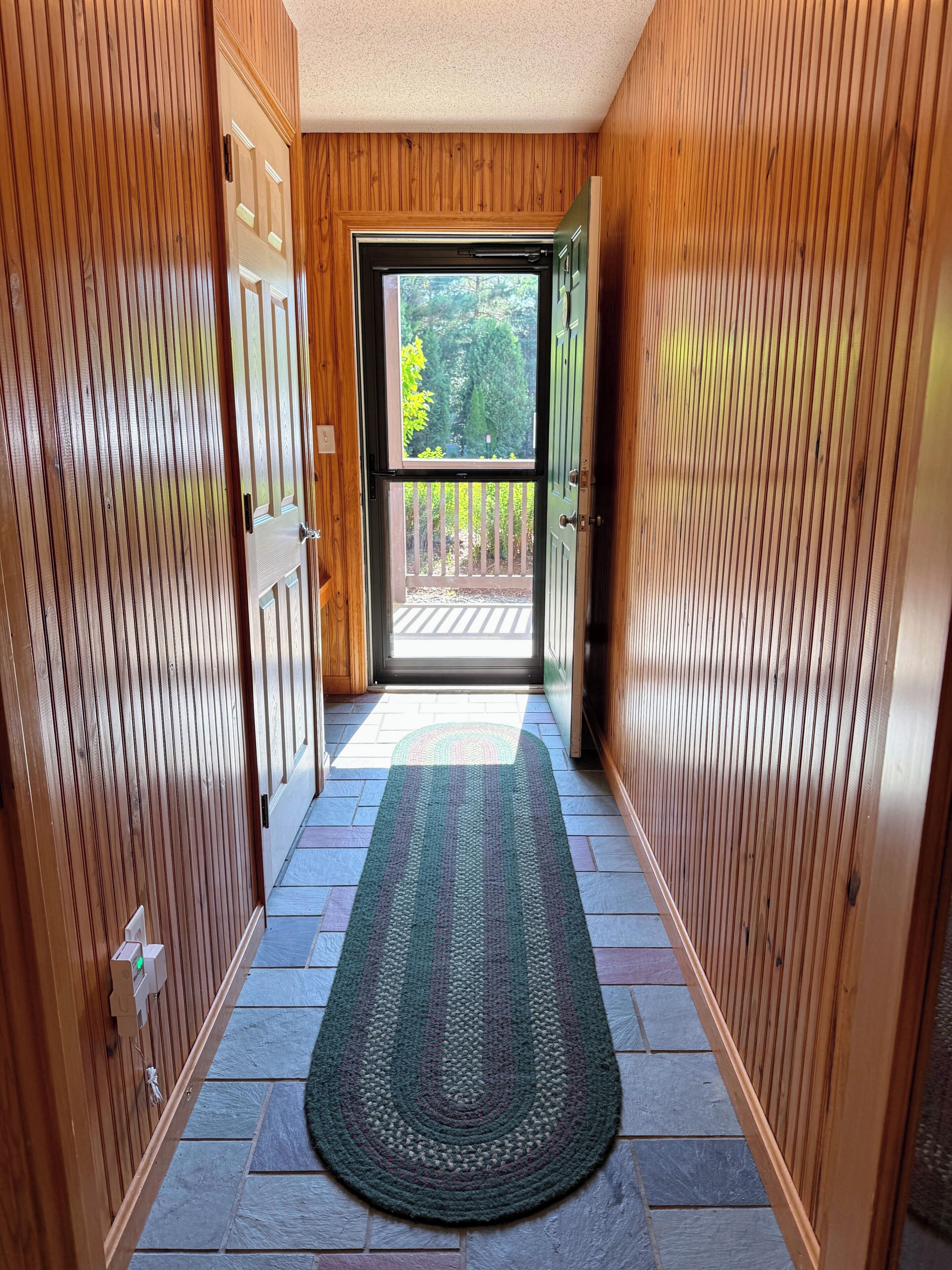 A wooden hallway with a rug leading to a glass door.