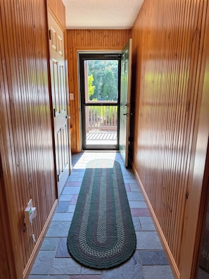 A wooden hallway with a rug leading to a glass door.