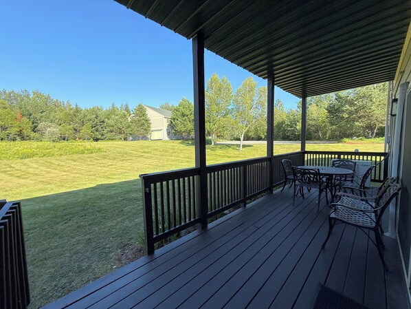 A covered outdoor area with a wooden deck, metal chairs, and a table.