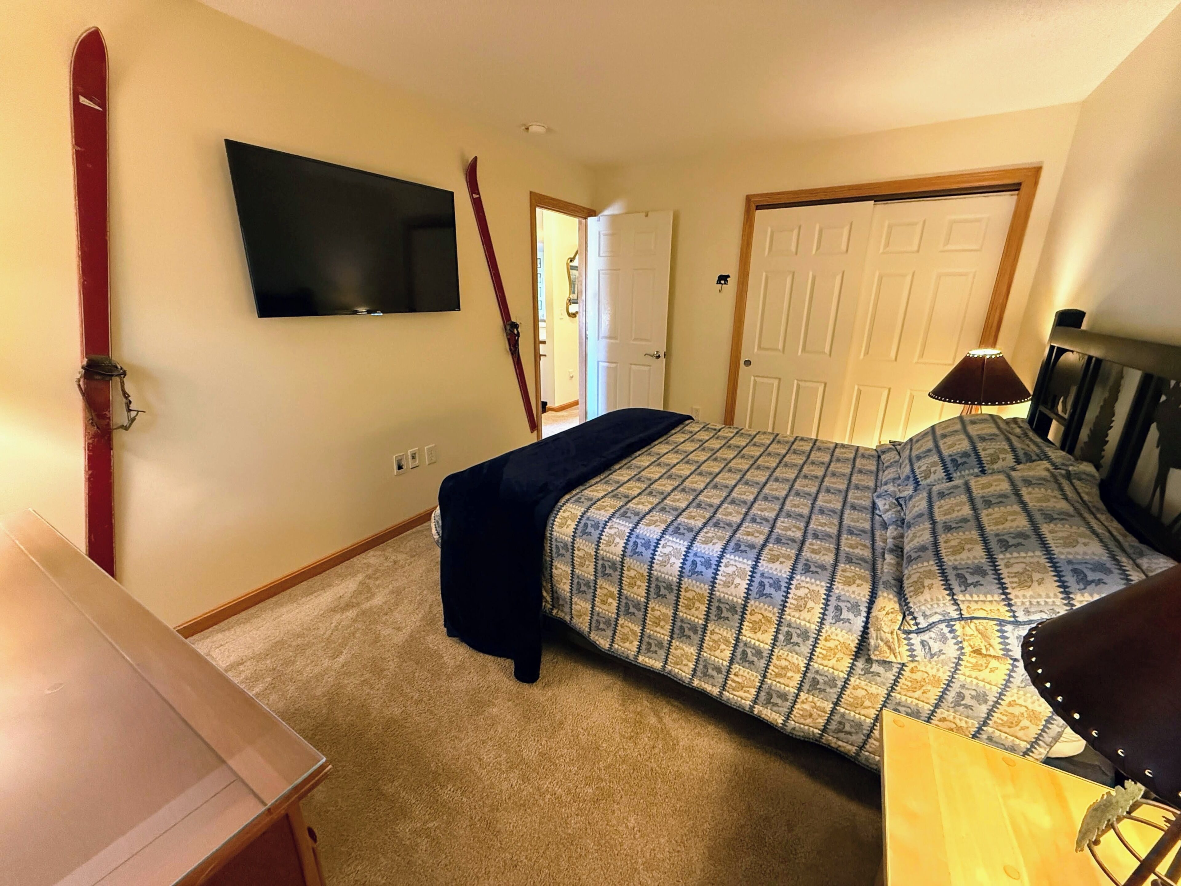 A bedroom with a bed, a TV mounted on the wall, a door, and a lamp.
