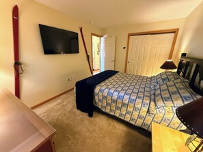 A bedroom with a bed, a TV mounted on the wall, a door, and a lamp.