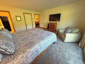 A bedroom with a large bed, a television, a chair, and a dresser.