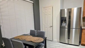 Een moderne keuken met een roestvrijstalen koelkast, een eettafel met stoelen en een raam met jaloezieën.