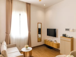 Ein modernes Hotelzimmer mit einer Couch, einem kleinen runden Tisch mit einer Vase, einem Fernseher, einem Holzschrank und einem Spiegel.