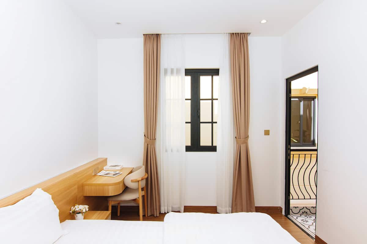 Ein Hotelzimmer mit Bett, Schreibtisch und Stuhl. Ein Fenster mit Vorhängen und eine Tür zu einem Außenbereich.