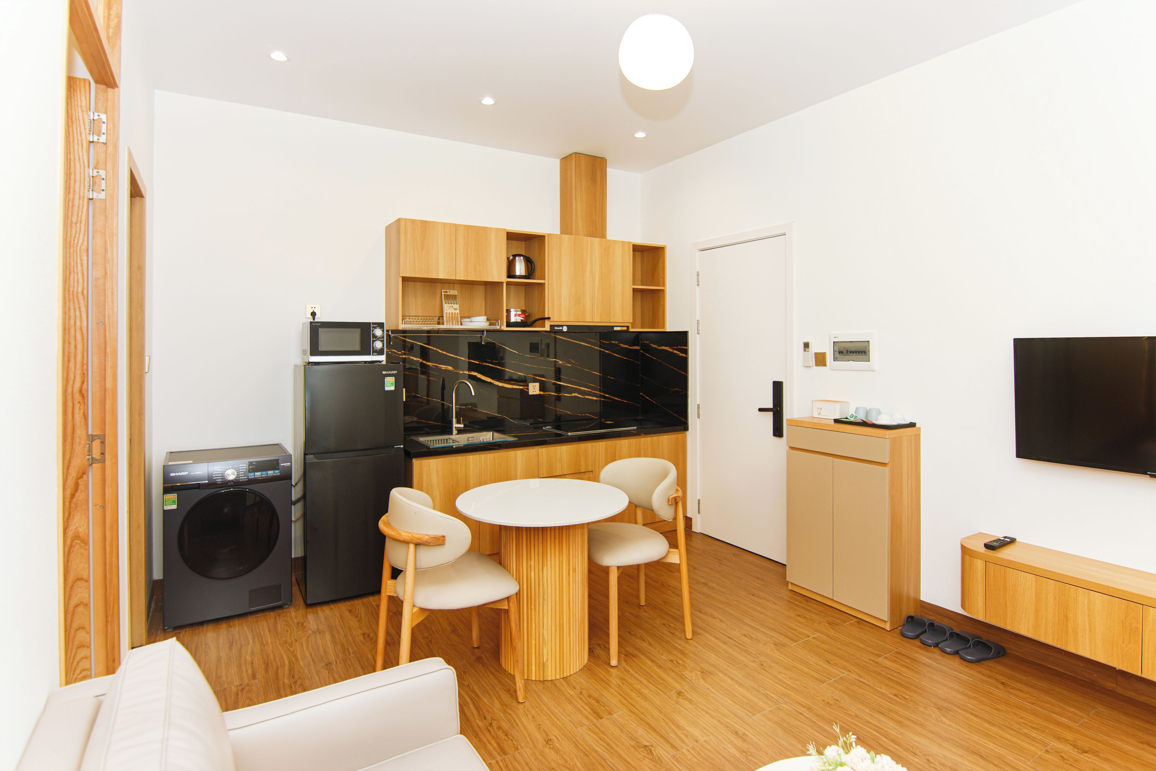 Un espacio habitable compacto con kitchenette, lavadora, comedor con mesa y sillas, sofá y televisor de pantalla plana montado en la pared.