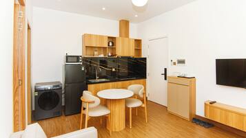Um espaço compacto com cozinha compacta, máquina de lavar, área de refeições com mesa e cadeiras, sofá e TV de tela plana na parede.