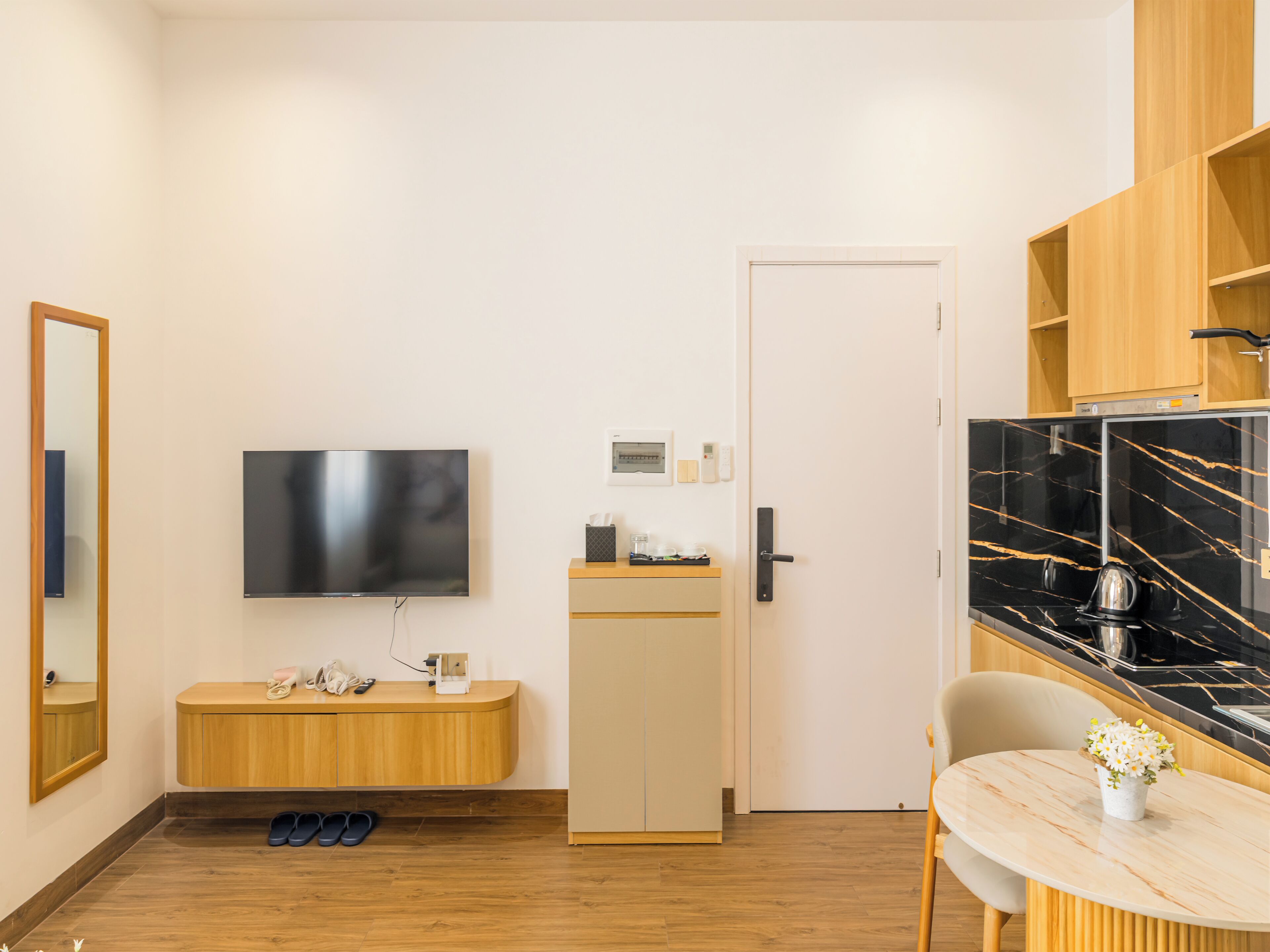 Een moderne hotelkamer met een flatscreen televisie, houten meubels, een kleine kitchenette en een eethoek.