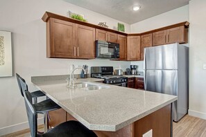 A kitchen with brown cabinets, a stainless steel refrigerator, a microwave, and a stove. - Chic & Modern 2BR Condo (Salt Lake City)