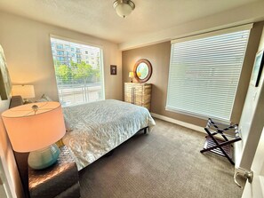 A bedroom with a bed, a lamp, a dresser, a window with blinds, and a hanging chair. - Chic & Modern 2BR Condo (Salt Lake City)