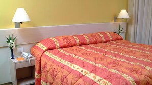 A hotel room with a bed, bedside lamps, a telephone, and a vase with flowers.