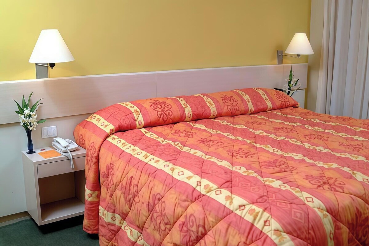 A hotel room with a bed, bedside lamps, a telephone, and a vase with flowers.