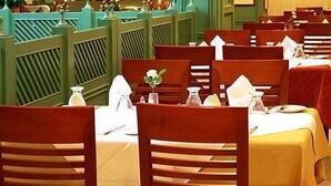 A restaurant with wooden chairs and tables, some with white tablecloths.