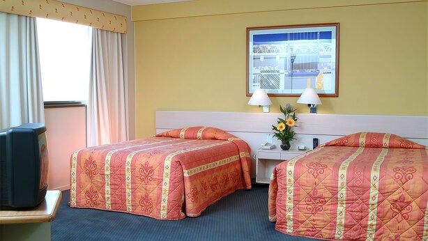 A hotel room with two beds, a desk, a television, and a window with curtains.