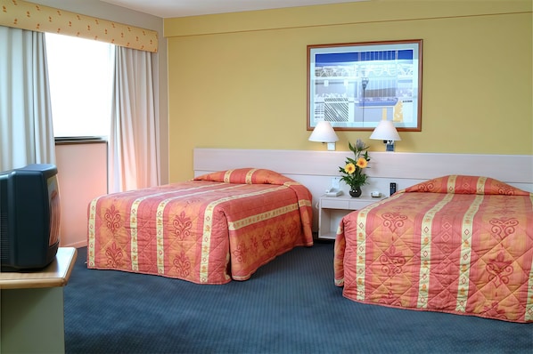 Habitación de hotel con dos camas, un escritorio, televisor y ventana con cortinas.