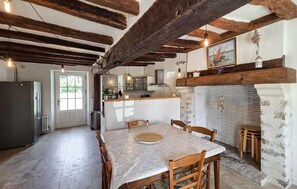 A rustic kitchen with exposed wooden beams, a dining table with chairs, and a fireplace. - Nice home in Manthelan (Manthelan)